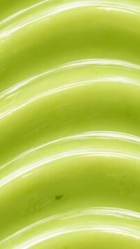 Abstract portrait background pattern of smooth creamy avocado dip with wavy ridges. Macro extreme close up of glossy green avocado paste swirl texture.
