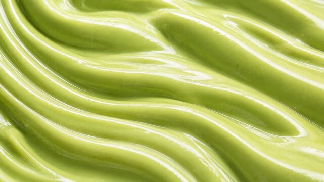 Macro extreme close up of glossy green avocado paste swirl texture. Abstract background pattern of smooth creamy avocado dip with wavy ridges.