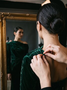 Close-up behind-the-scenes photograph of a professional fashion model being styled by a fashion professional, only hands of the stylist visible adjusting an elegant premium garment