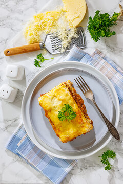 Lasagne mit Hackfleisch prepared in popular German style with layered ground beef and melted cheese served on a grey plate on a marble background, vertical, not AI
