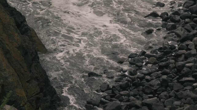 Waves crashing violently against numerous rounded stones along a rocky shore
