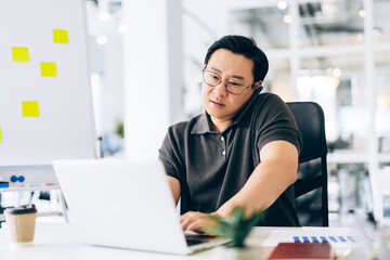 Fototapeta premium Busy asian man multitasking with laptop and smartphone in modern office