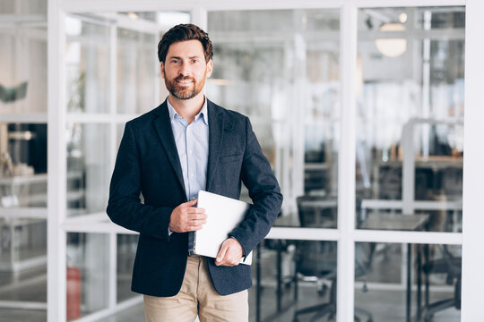 Confident businessman holding laptop standing in modern office