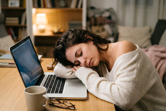 Young woman sleeping at desk while working on laptop at home
