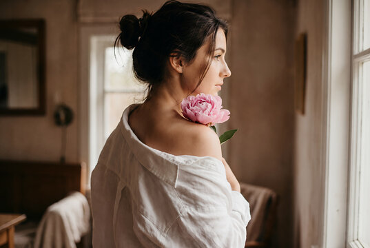 Young Asian woman holding pink peony flower by window