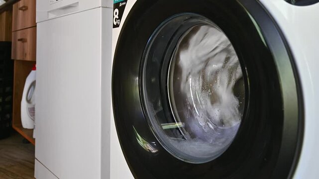 Close-up wash a bed linen in a laundry drum in a washing machine in a small hotel or hostel.
