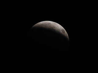 Partial lunar eclipse showing the Earth’s shadow moving across the surface of the Moon against a dark night sky. © Dmytro