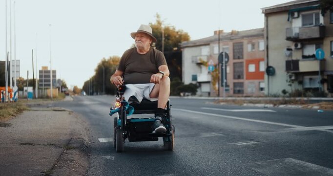 Front view of a senior man in an electric wheelchair arriving at a traffic light and stopping to wait at a city crossing during his independent daily routine.