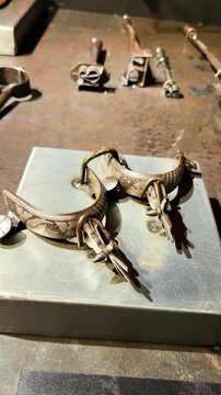 Antique cowboy spurs with engraved metal surfaces and rowels displayed on workshop table, vertical
