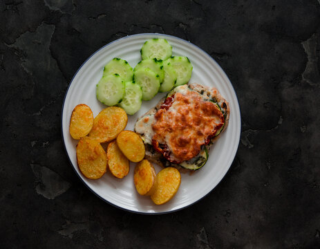 Baked meat chop with zucchini, tomato, mozzarella, baby potatoes, cucumber - a delicious balanced lunch on a dark background, top view