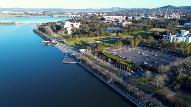 Drone aerial landscape of the waterfront promenade foreshore and local pathway with a flag display and public carpark at Lake Burley Griffin in Parkes Canberra ACT Australia tourism and infrastructure