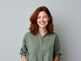 Obraz premium Portrait of a smiling young woman with red hair wearing a green shirt, looking at the camera against a plain grey studio background