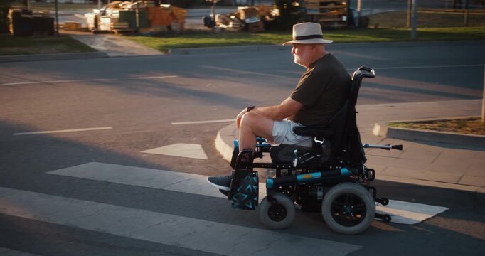Senior man in an electric wheelchair waits at a crosswalk and then continues through the city, showing independent mobility and accessible everyday life in an urban setting.
