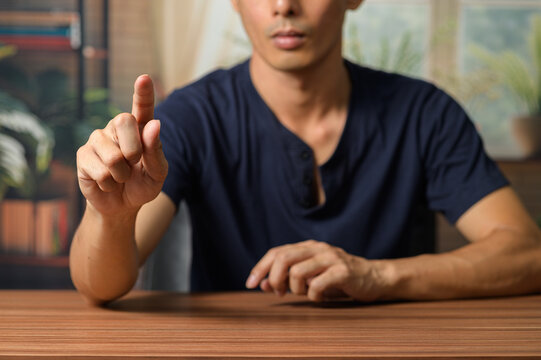 Focused Man Gestures with Finger While Sitting at Wooden Table