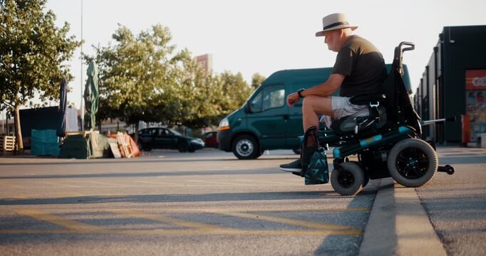 Senior man in an electric wheelchair carefully and successfully crosses a curb in the city, highlighting everyday mobility barriers and limited accessibility for wheelchair users.