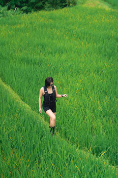 Young woman walking through lush green rice field path in rural outdoor natural landscape during daytime