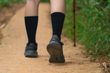 Naklejka premium Close-up of woman leg walking on dirt trail wearing black socks and athletic shoes with hiking stick support in nature