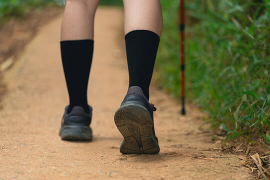 Close-up of woman leg walking on dirt trail wearing black socks and athletic shoes with hiking stick support in nature