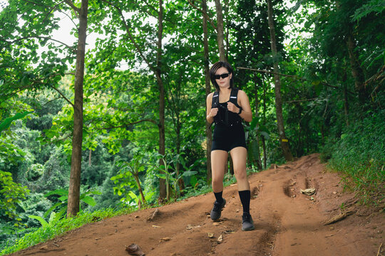 Woman hiking alone on dirt trail in dense green forest wearing black outfit and sunglasses during day