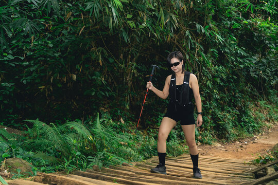 Woman with black outfit and sunglasses hiking on wooden path surrounded by lush green forest vegetation in daytime