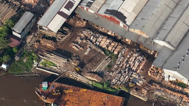 Stacks of raw logs and processed wood arranged at an industrial timber site beside a river