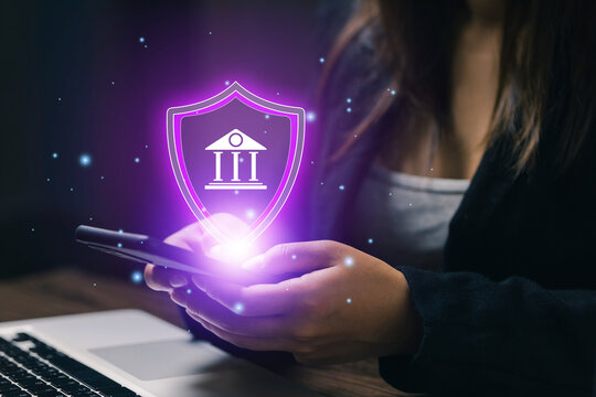 Businesswoman using smartphone with glowing bank security shield icon, illustrating secure mobile banking, financial protection, digital payment, fintech and online account safety.
