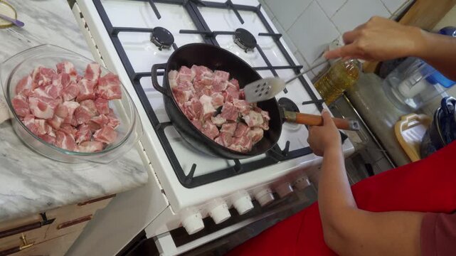 A close-up of frying pork cubes in a glass bowl on a gas stove in a kitchen setting, captured from a first-person perspective. The scene is set with a red shirt person nearby, emphasizing.