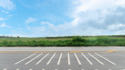 Naklejka premium Horizontal or landscape view of asphalt road featuring white chevron pavement markings.Speed ​​bump lines. On the wet road surface in the side lane. Alongside green grass under a cloudy blue sky.