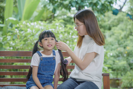 Happy family beautiful mother woman brushing her daughter hair while sitting outdoor at home