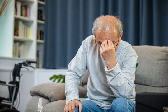 Asian mature old man sitting on sofa headache at home in living room, Depressed senior man unhappy hands rubbing eye suffering from a migraine