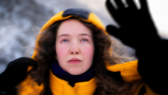 Female mountaineer shielding her face from strong wind and blowing snow during a challenging winter ascent in the mountains.
