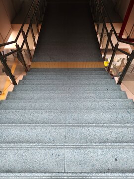 Urban architectural low angle view of an ascending wide granite staircase with black non-slip treads, leading to an unknown destination.