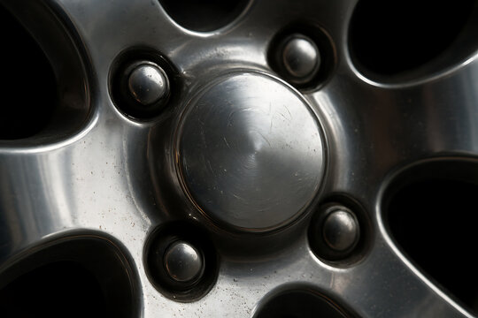 Close-up of shiny metal wheel rim with lug nuts and reflective surface