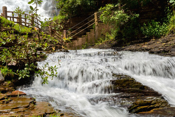 A magnificent sight of the milky waterfall cascaded down over the rocky hill amid the green...