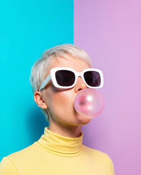 Adult Model in Retro Sunglasses Blowing Bubblegum against Split-Color Studio Wall