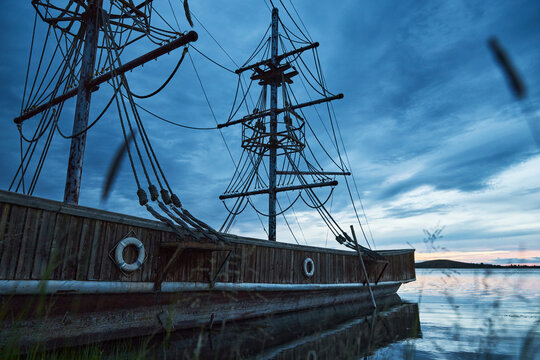 Blue-toned twilight lakeside landscape with antique-style wooden two-masted sailboats moored on the lake.
