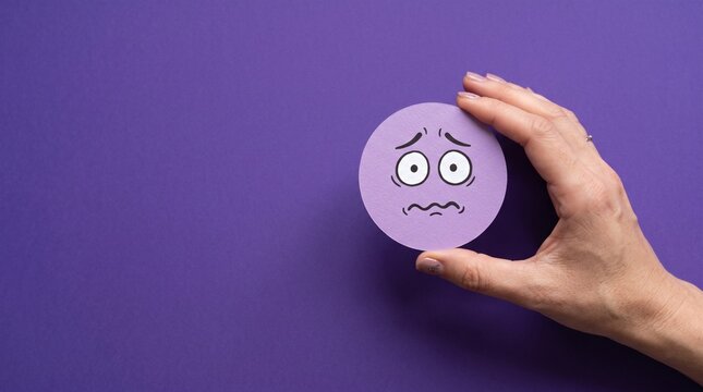 Hand holding a circular purple paper cutout displaying an anxious facial expression representing stress and emotional discomfort in daily life