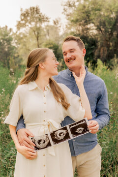 Joyful expecting couple holding baby ultrasound scan photos outdoors
