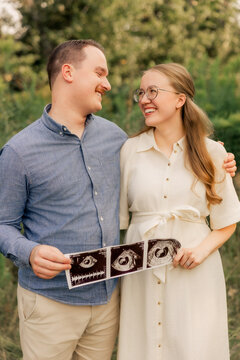 Happy expecting couple looking at each other holding sonogram photos