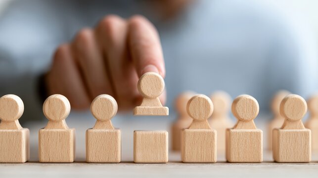 Wooden figures arranged in a row, one figure carefully being lifted, symbolizing teamwork, leadership, and selection process concepts for business
