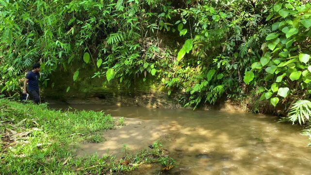 Lone explorer discovering remote forest creek while walking barefoot upstream in Amazon alike rainforest.