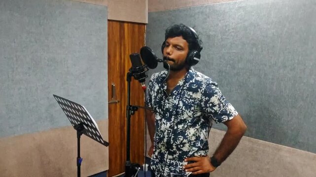 male voice artist wearing headphones and recording film dialogue into a professional condenser microphone with a pop filter at hyderabad, telangana, india. internal shot, hand held shot, 4k.