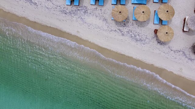 Turquoise Mediterranean Beach with Straw Umbrellas and Blue Loungers in Halkidiki Greece Aerial Brids Eye View