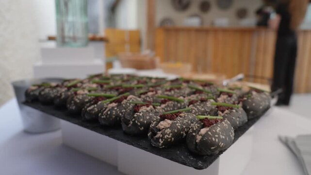 Black sesame rolls filled with savory spreads and chives line a wedding buffet platter
