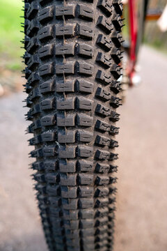 Extreme close-up of a bicycle tire tread with knobby pattern on a blurred road background. Concept of mountain bike maintenance, cycling equipment, grip, tire pressure, and outdoor adventure sports.