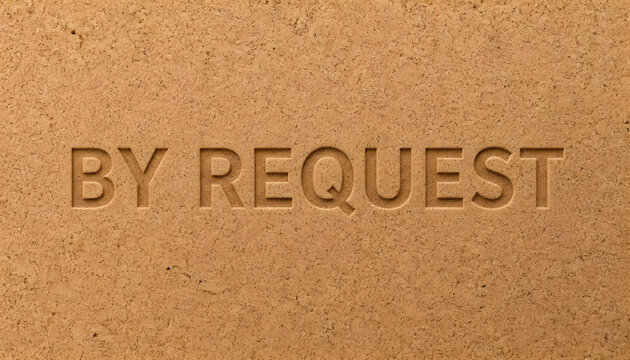 Engraved word By Request carved into textured cork board surface