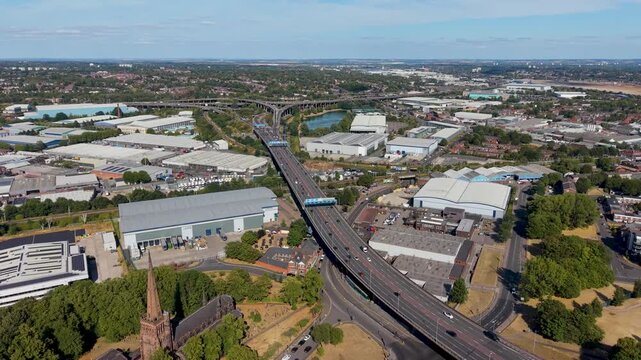 Spaghetti junction Birmingham aerial reverses away from the M6 Gravelly Hill Interchange, revealing flyovers, traffic flow, warehouses, canals and urban sprawl under summer sky.