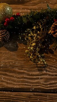 Animation of christmas baubles decoration with snow falling on wood