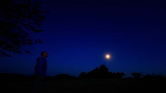 Silhouette of a person in nature observing night sky, Moon, stars and planets from a remote location.