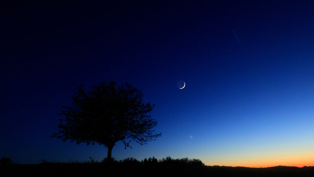 Moon on a twilight sky with stars, planets and landscape mountain silhouettes.